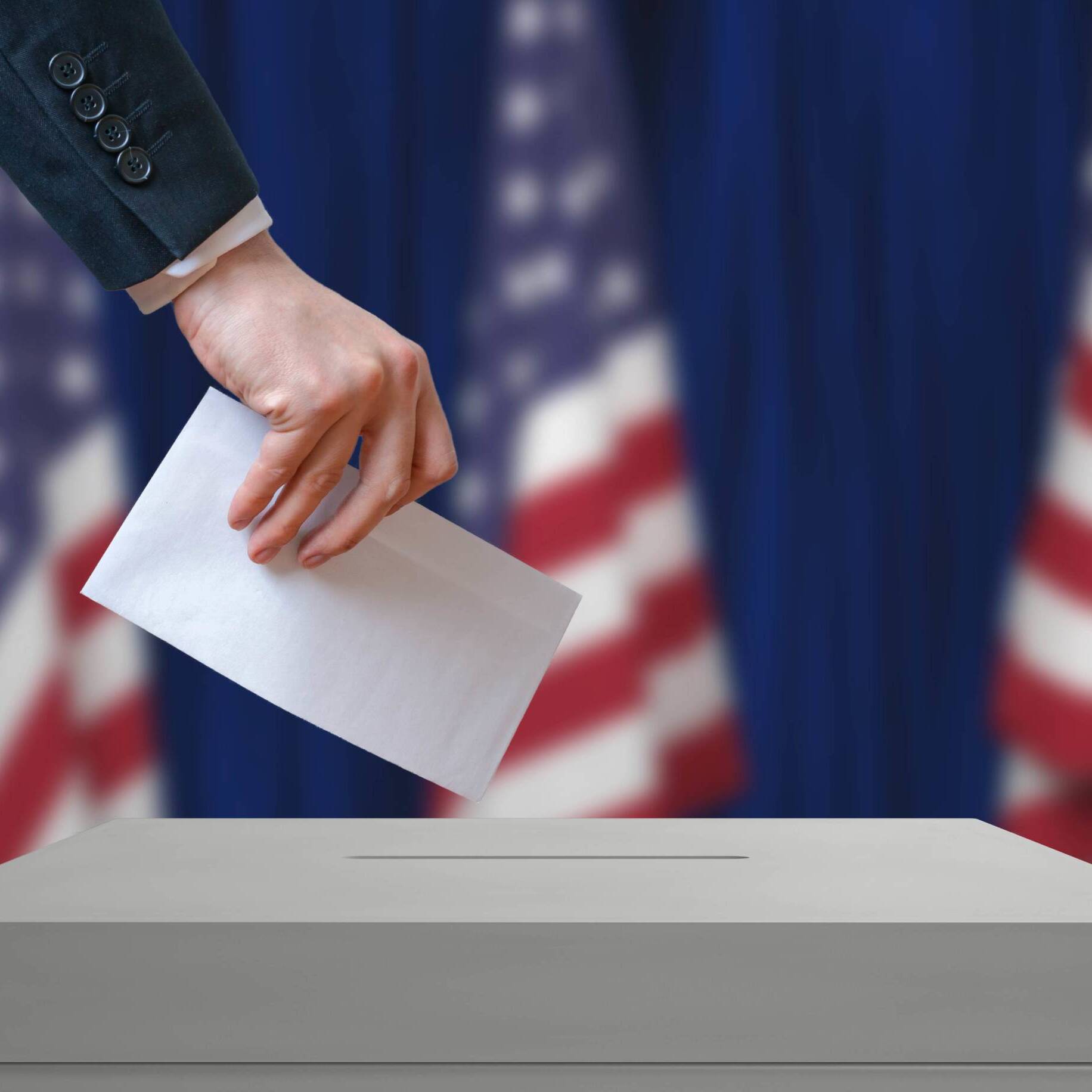 Election in United States of America. Voter holds envelope in hand above vote ballot. USA flags in background. Democracy concept.