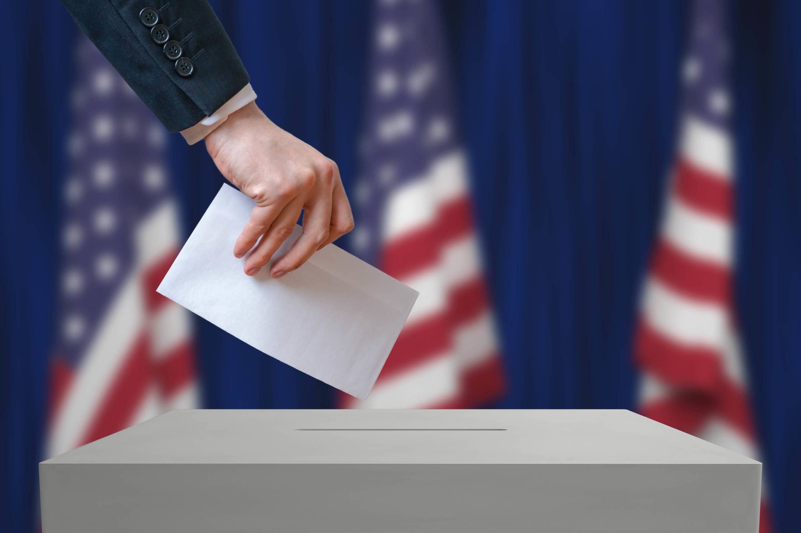 Election in United States of America. Voter holds envelope in hand above vote ballot. USA flags in background. Democracy concept.