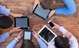 Men and women Staring Intensively on Screens of Digital Gadgets Natural Rough Wooden Plank Desk and Four People Holding Working Electronic Devices Tablet PC Book Notepad Smart Telephone