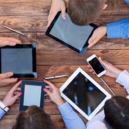 Men and women Staring Intensively on Screens of Digital Gadgets Natural Rough Wooden Plank Desk and Four People Holding Working Electronic Devices Tablet PC Book Notepad Smart Telephone