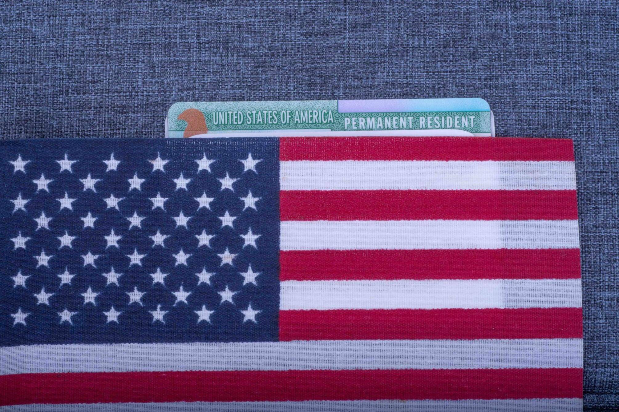 Green Permanent resident card covered American (USA) flag on light blue fabric surface.