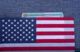 Green Permanent resident card covered American (USA) flag on light blue fabric surface.