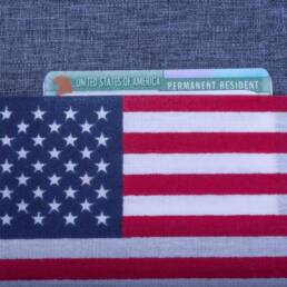 Green Permanent resident card covered American (USA) flag on light blue fabric surface.