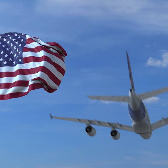 Commercial airplane landing behind waving American flag. Travel to the United States conceptual 3D rendering